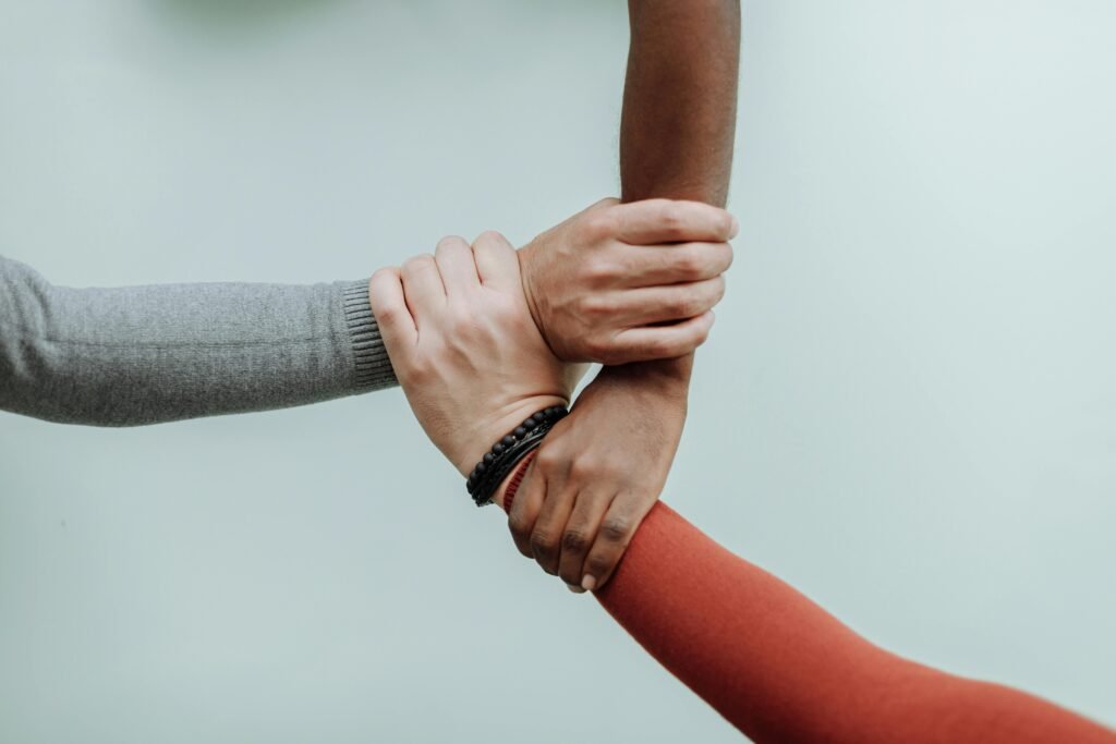Three people of different backgrounds grasping each other’s wrists in a supportive triangle, symbolizing mutual support and connection.