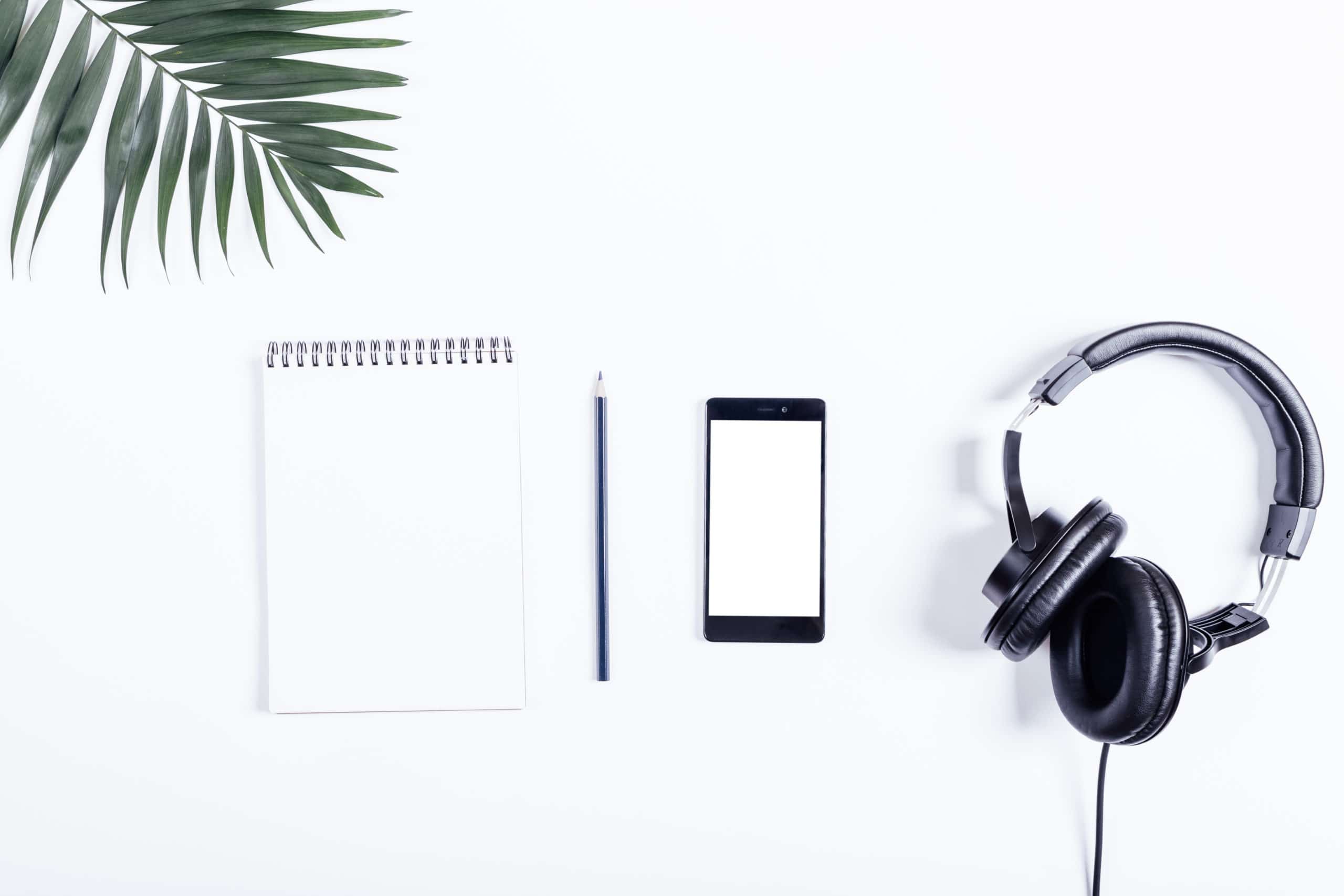 Mobile phone, black headphones, notebook, pencil and green leave